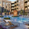 A modern apartment complex in Oklahoma City features a central outdoor pool area surrounded by lounge chairs, greenery, and a water feature.