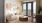 A modern living room in one The Residences at OAK, featuring a beige sofa, wooden coffee table, large windows with a city view, patterned rug, framed abstract art, and a wooden chair with cushions.